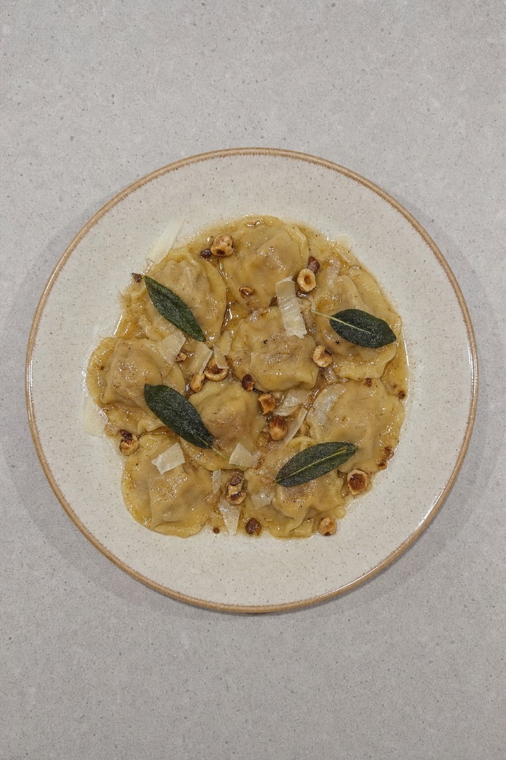 Foto zenital sencilla de un plato de agnolotti sobre una encimera neutra, con luz doméstica plana.